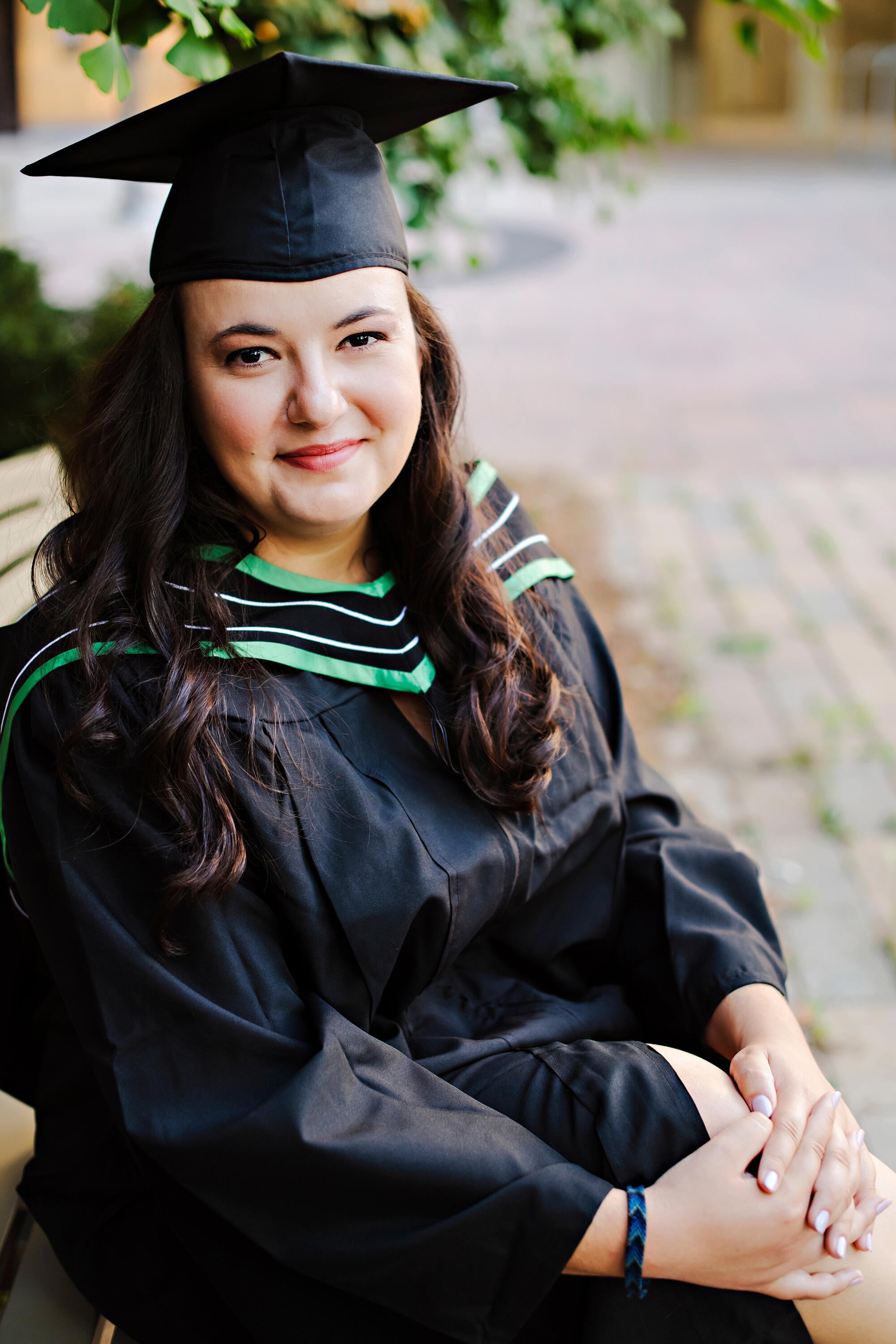 student wearing cap and gown poses while seated on a bench