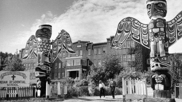archival image of residential school with totem poles in front of old building