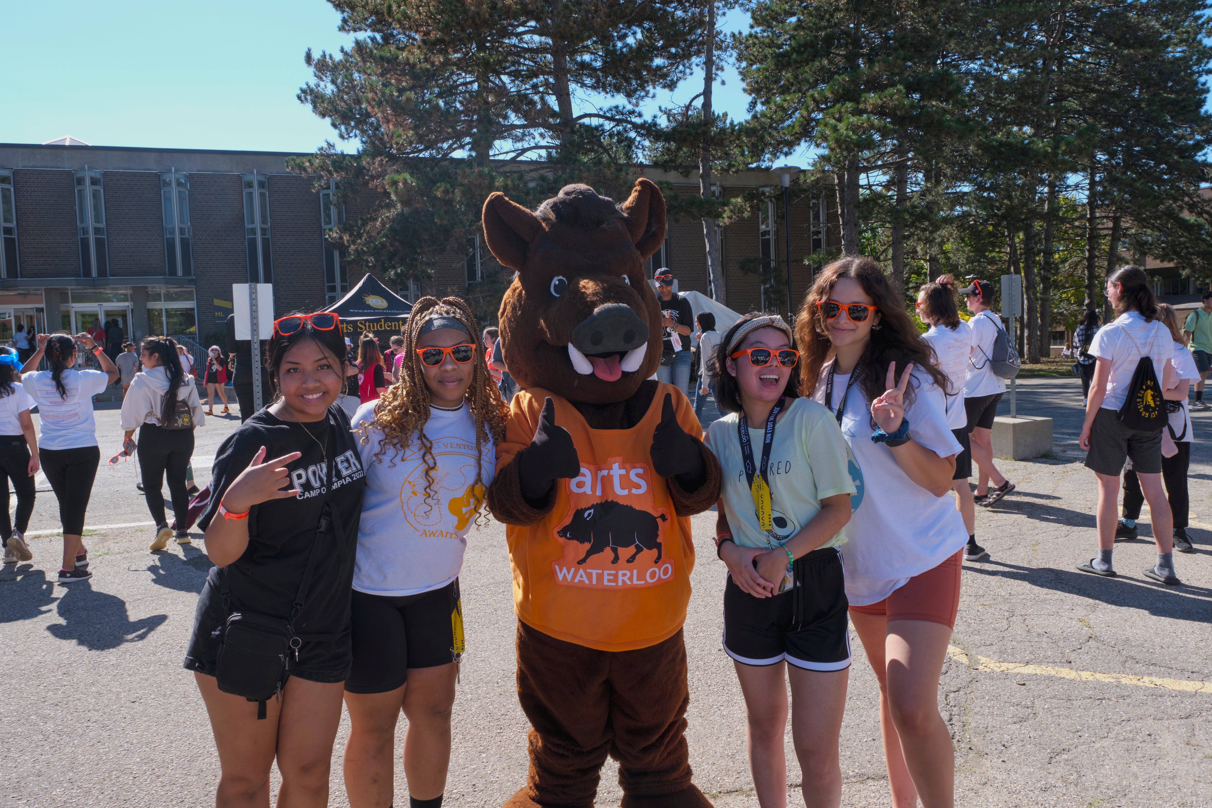four smiling students in orange sunglasses with boar mascot