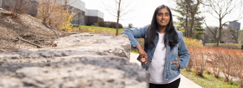 Student leaning on rock wall with phone in her hand