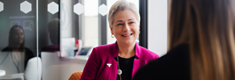 Norah McRae sitting, smiling wearing a pink blazer and a University of Waterloo pin