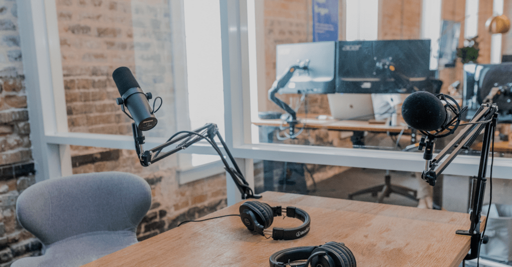 Office with brick walls featuring a desk with podcast microphones and headphones sitting on it.