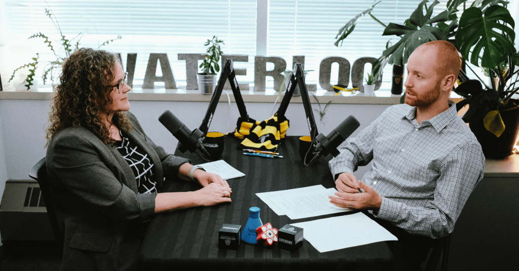 Jodi Szimanski (left) and David Drewery (right) sitting in a bright room with plants and microphones.