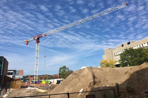 construction crane with blue sky behind and dirt pile with construction fencing in foreground