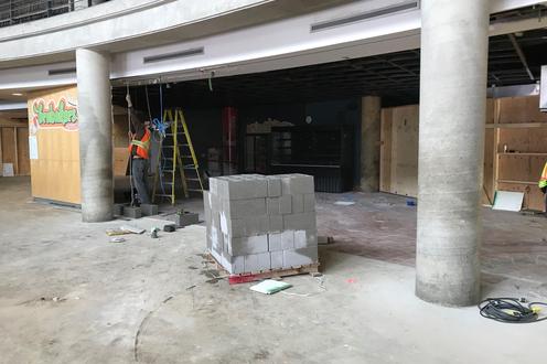 A flat of cement blocks and a construction worker in the background in the space that was the dining hall and Brubakers
