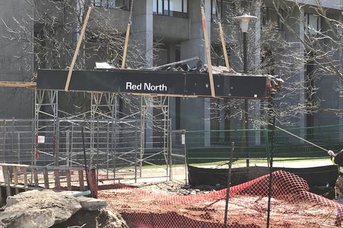 A steel beam with Red North in white letters is lifted from a construction site