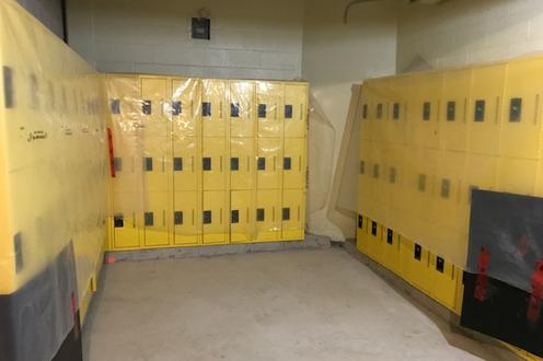 Banks of yellow lockers covered in plastic wrap in a room with concrete floors.