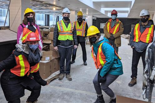 Athletics team wearing safety hats and vests, getting a tour of the new space.