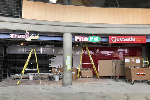 Partially complete dining area with concrete floors, tile walls and signage for food services Shawarma hub, Pita Pit, Quesada.