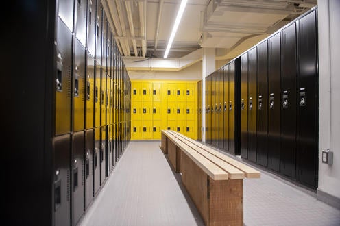 Wooden bench in middle of a change room with shiny black lockers in foreground and yellow lockers in background