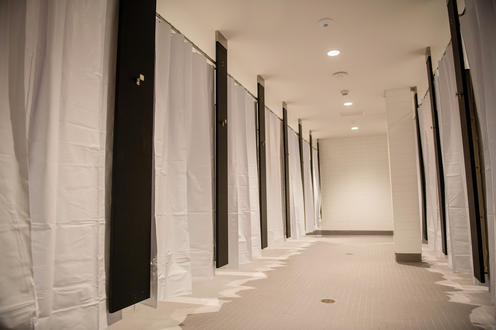 A long room with several shower stalls each with a white shower curtain.