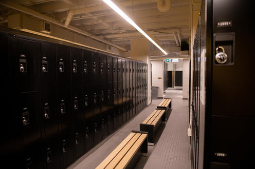 Row of black lockers stacked 3 high on either side and benches in the middle.