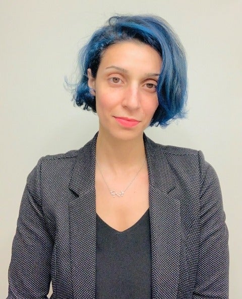 headshot of a person with short blue hair, black top and grey blazer