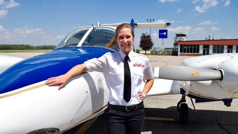 Young female pilot smiling in front of a small plane