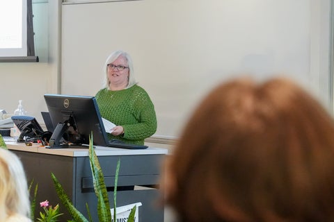 A woman speaking at the front of a lecture hall. 