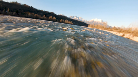 An Arial shot from a drone flying over a river with mountains in the background 