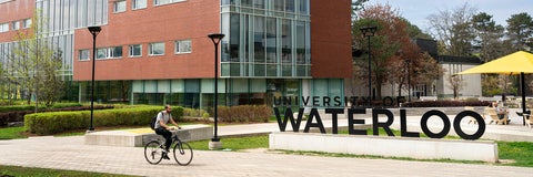 Cyclist riding on main path in front of the University of Waterloo Sign