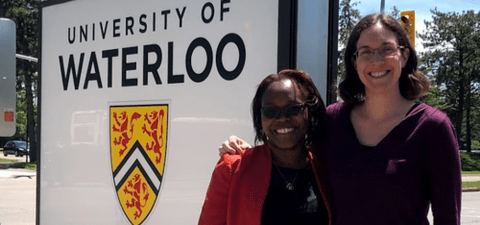 Prof. Laura Hug and female colleague stand by University of Waterloo sign.