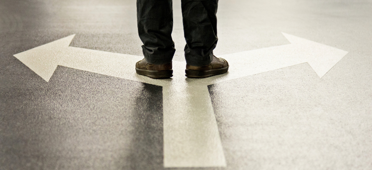 Stock image of feet standing on the intersection of an arrow pointing right and an arrow pointing left.