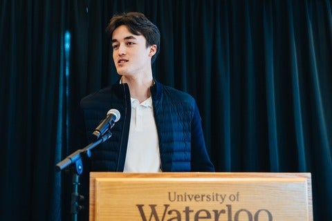 Jarett Dewbury standing in front of University of Waterloo podium speaking into a microphone
