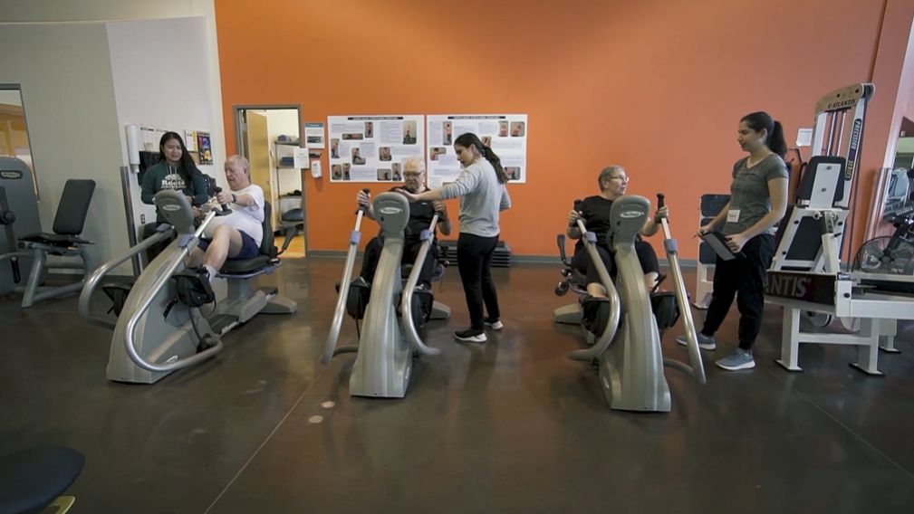 volunteers working with participants on recumbent bicycles at a gym