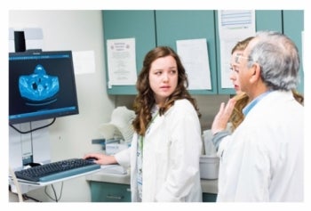Three researchers in lab coats discuss an image on a screen.