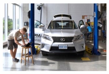Two students work on an SUV in a shop.