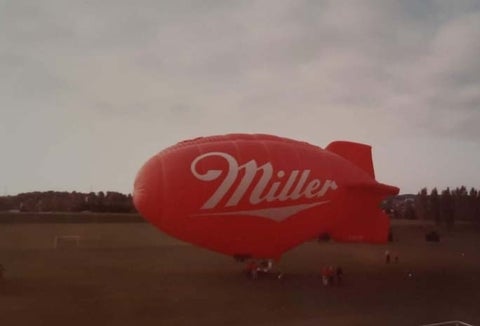 A red blimp with the Miller logo in white on the side gets ready to take off from Colombia lake fields.