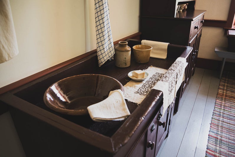 A wooden counter, with the top recessed to create an open shallow box. A face cloth, hand towel, soap, and bowl for washing sit whithin it.