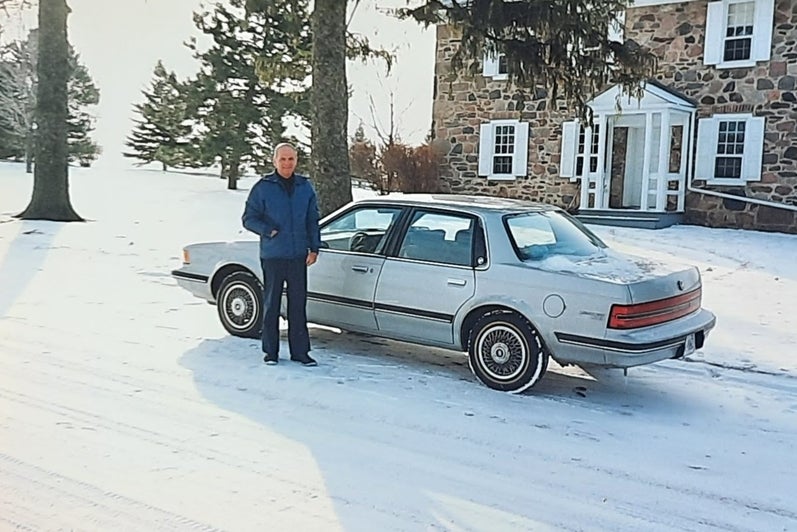 Howard stands beside a Buick in the snow, 1992