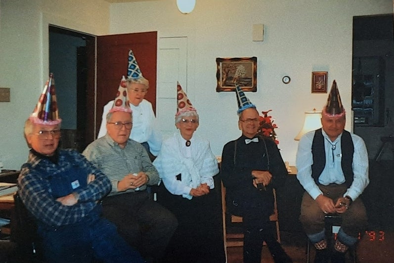 Six older adults sit in the Brubacher House living room wearing pointed decorative party hats, ready to celebrate the new year!