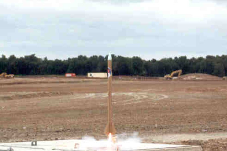 A small model rocket begins to take off off a concrete pad.