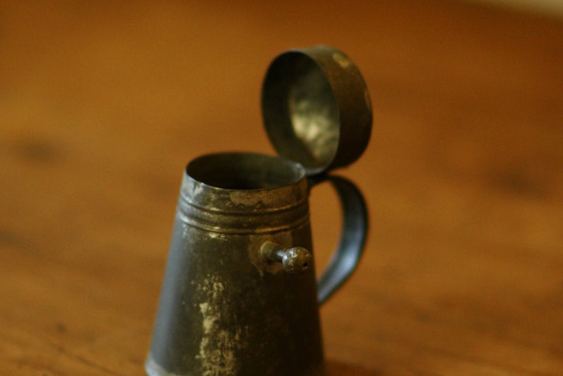 A tiny metal tankard shaped cup, with a lid on a hinge.