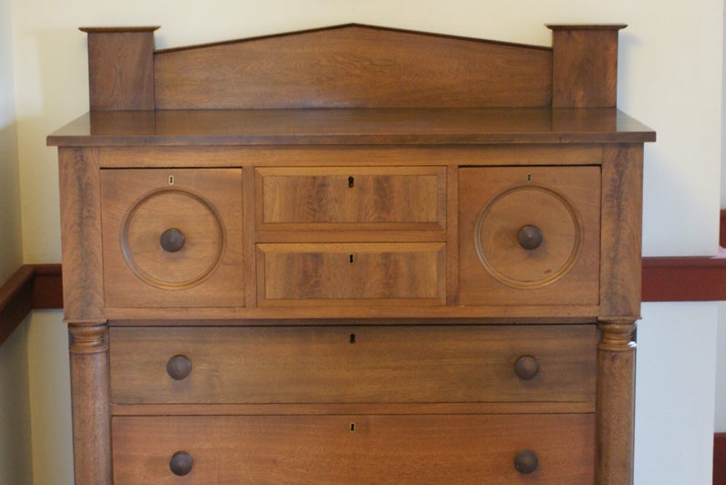 A large wooden dresser, with a small, rectangular mirror hanging above at a slight angle