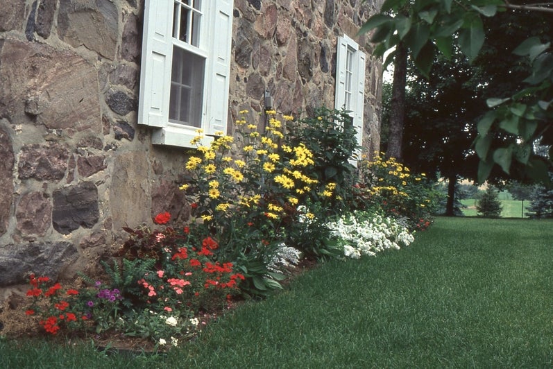 Red, pink, and large yellow flowers outside the stone walls