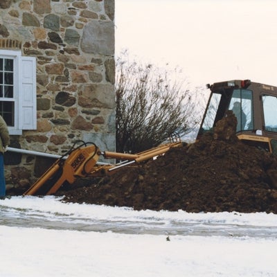 a backhoe digs into the foundation of Brubacher house for repairs