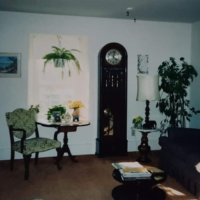 an old photo of the corner of a living room, a large standing clock stands prominently in the room.