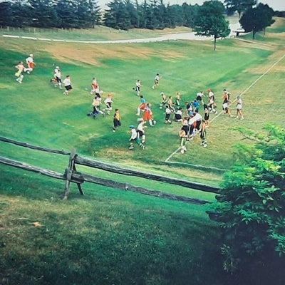 A group of kids in sports uniform run up and down the hill