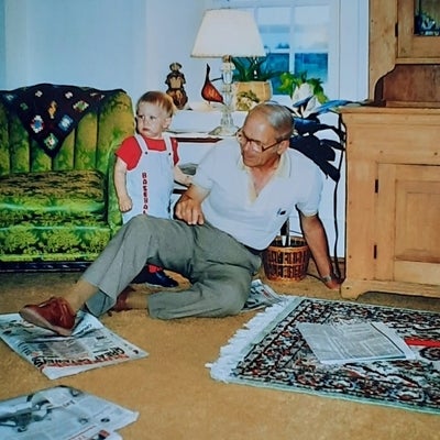 Howard sits on the floor with a young child, a variety of newspapers are on the floor of the living room.