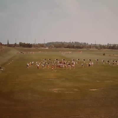 drum and bugle players practice in the field, in the distance.