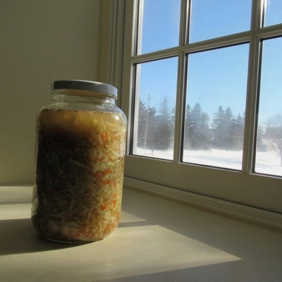 A mason jar of sauerkraut sits on the window sill, a winter scene outside.