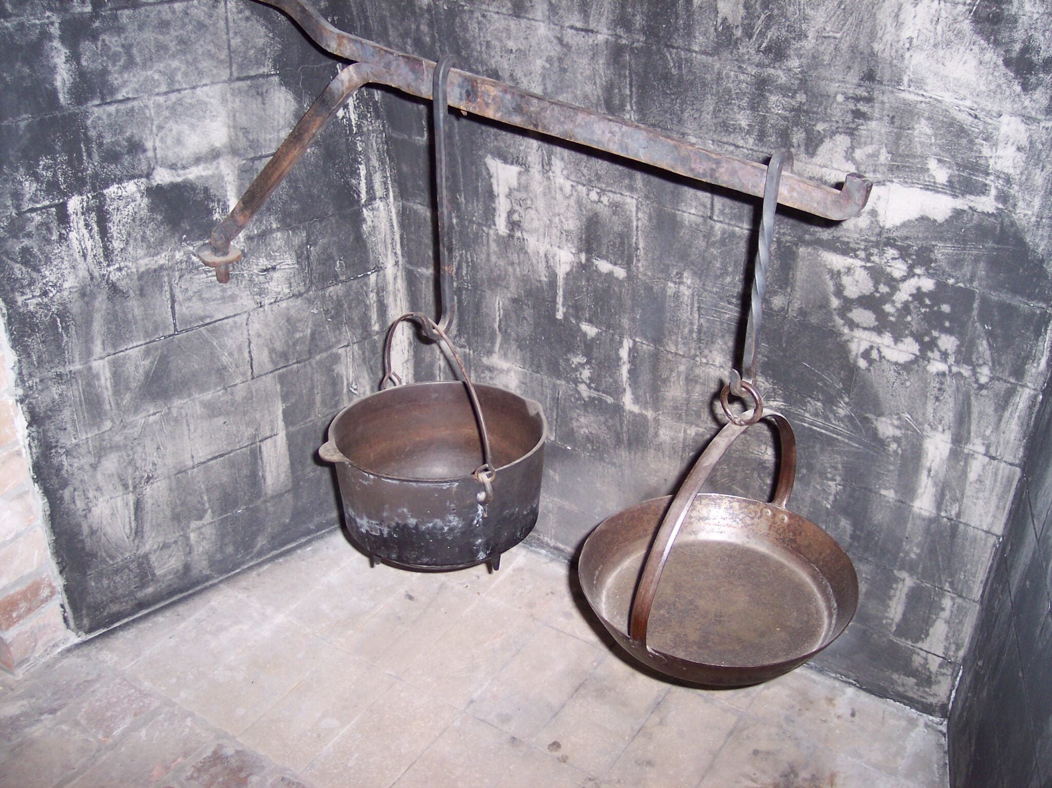 The view inside the open hearth fireplace, with brick covered in white ash, a cast iron cooking set hangs
