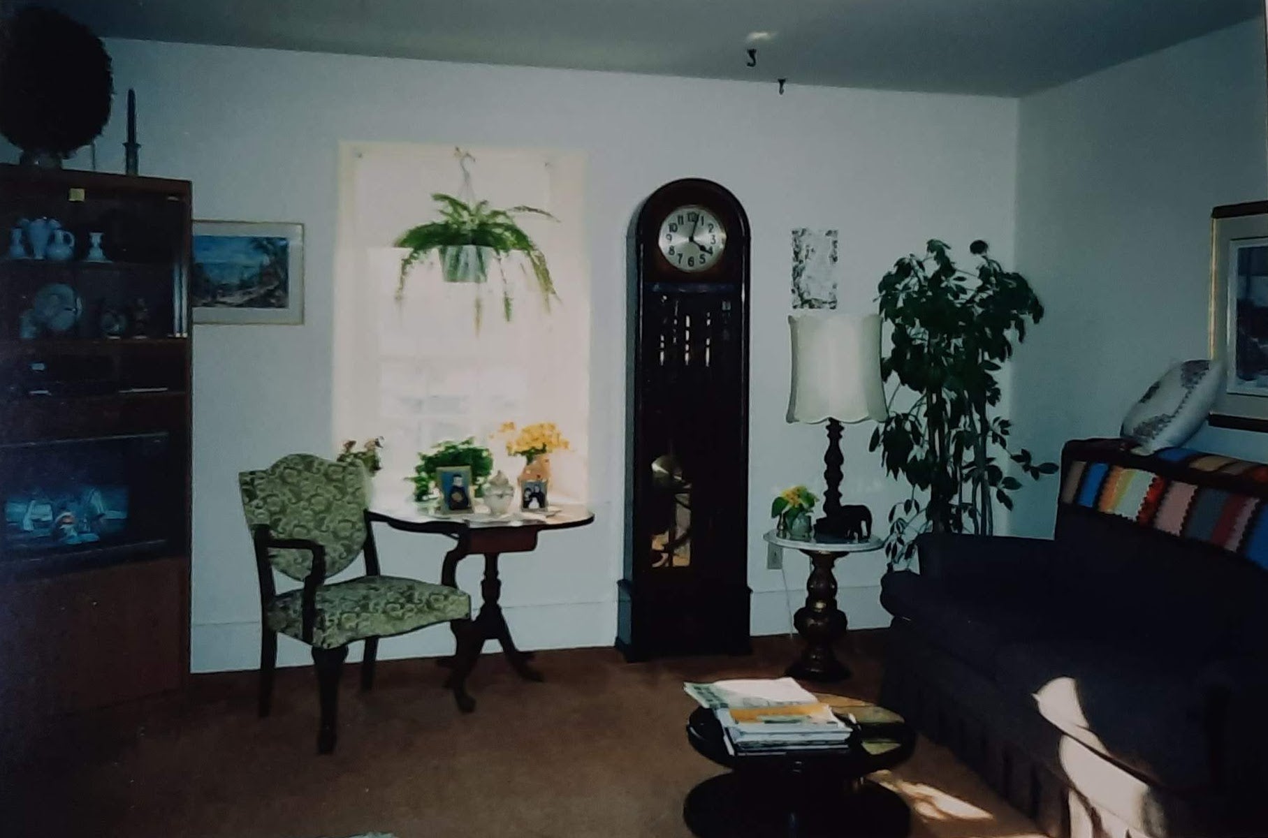 an old photo of the corner of a living room, a large standing clock stands prominently in the room.