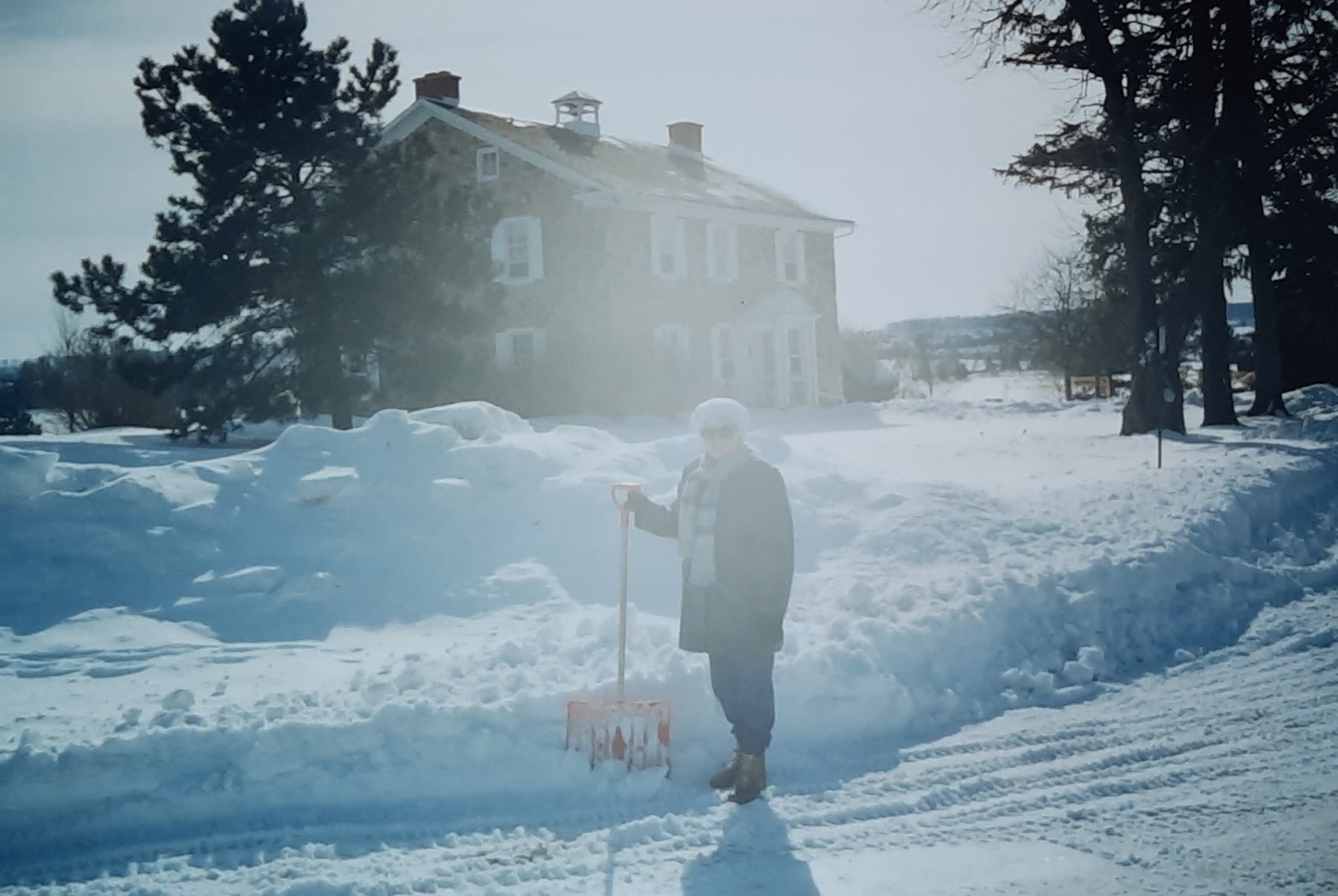Carol stands out front of Brubacher House in winter in 1994, with a snow shovel. There's a lot of snow!
