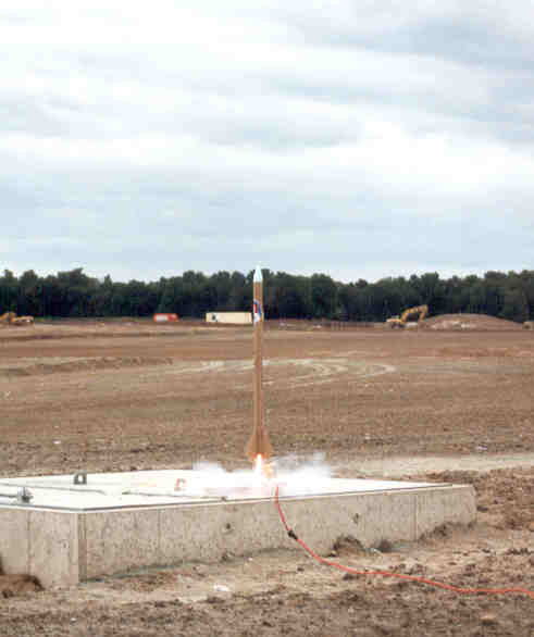 A small model rocket begins to take off off a concrete pad.