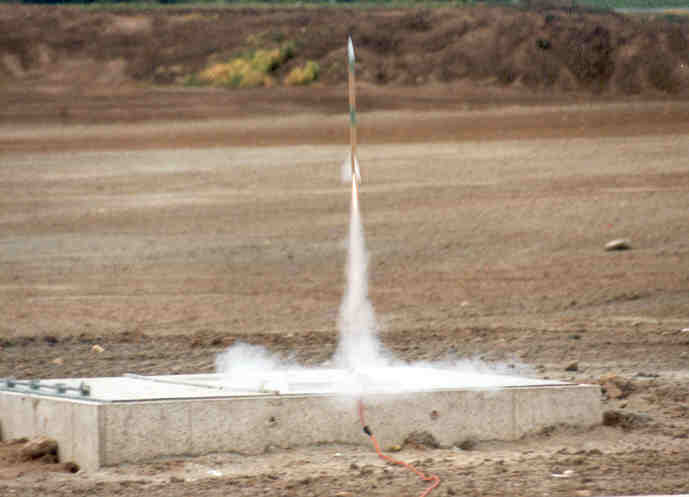 A small model rocket begins to take off off a concrete pad.