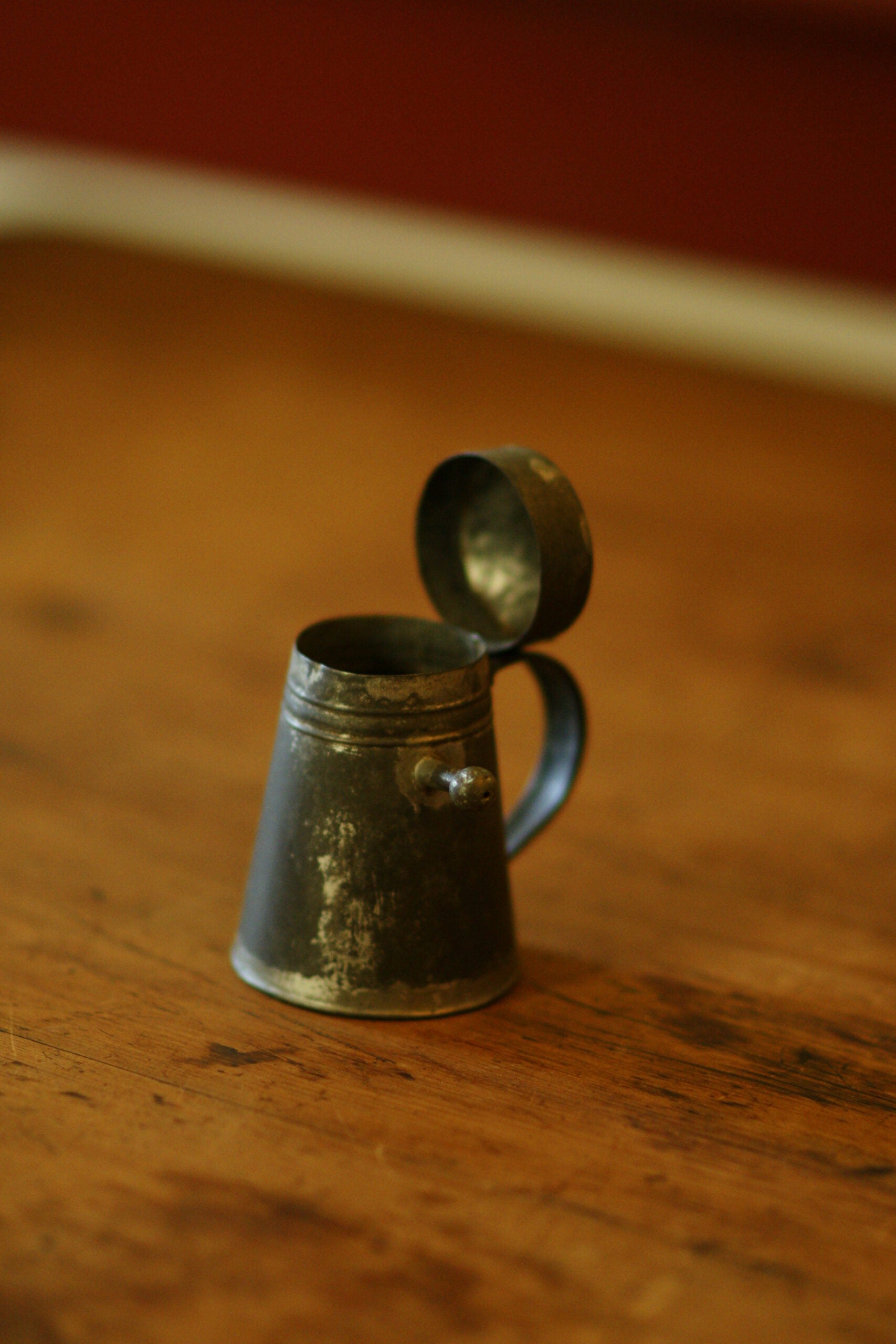 A tiny metal tankard shaped cup, with a lid on a hinge.