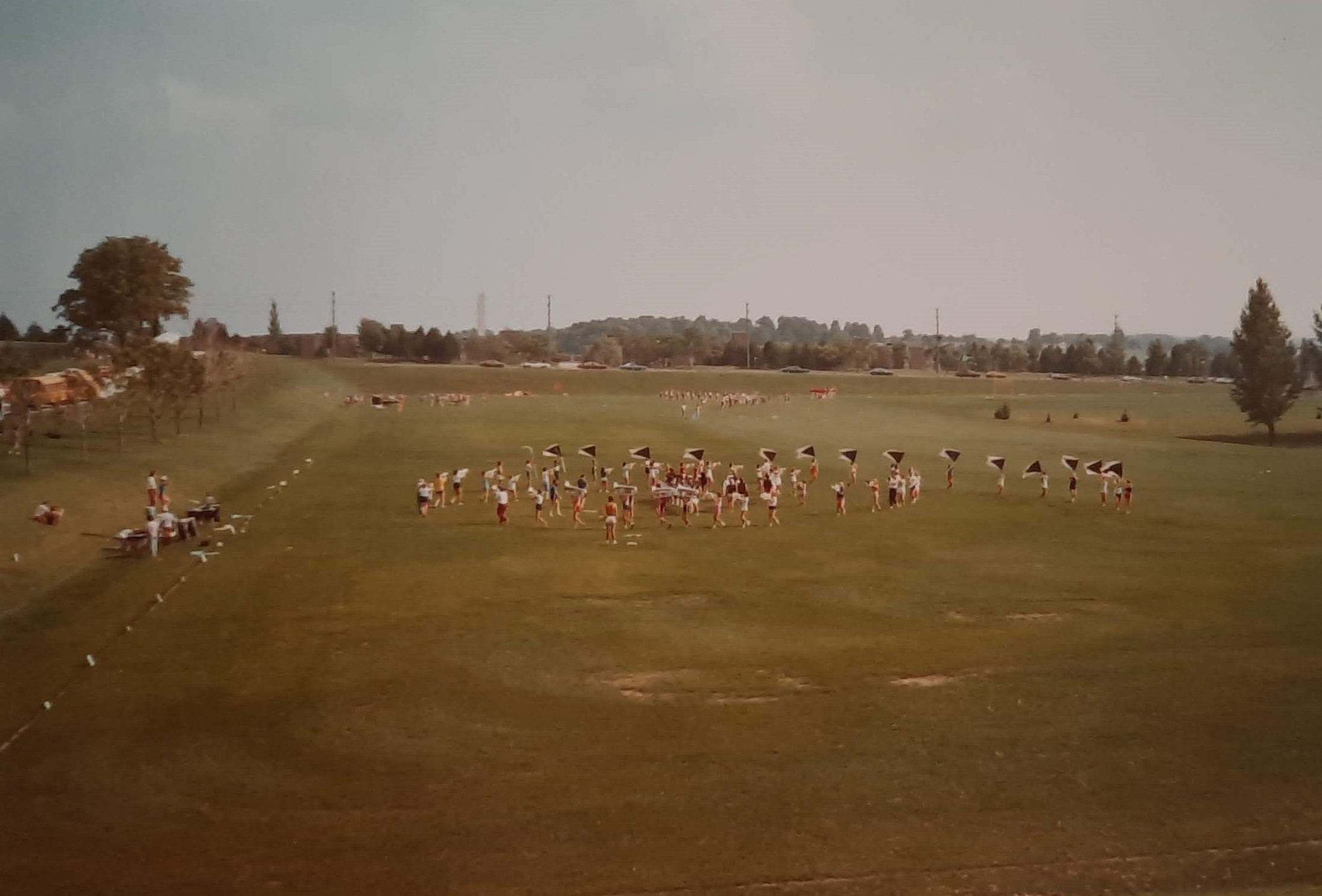 drum and bugle players practice in the field, in the distance.