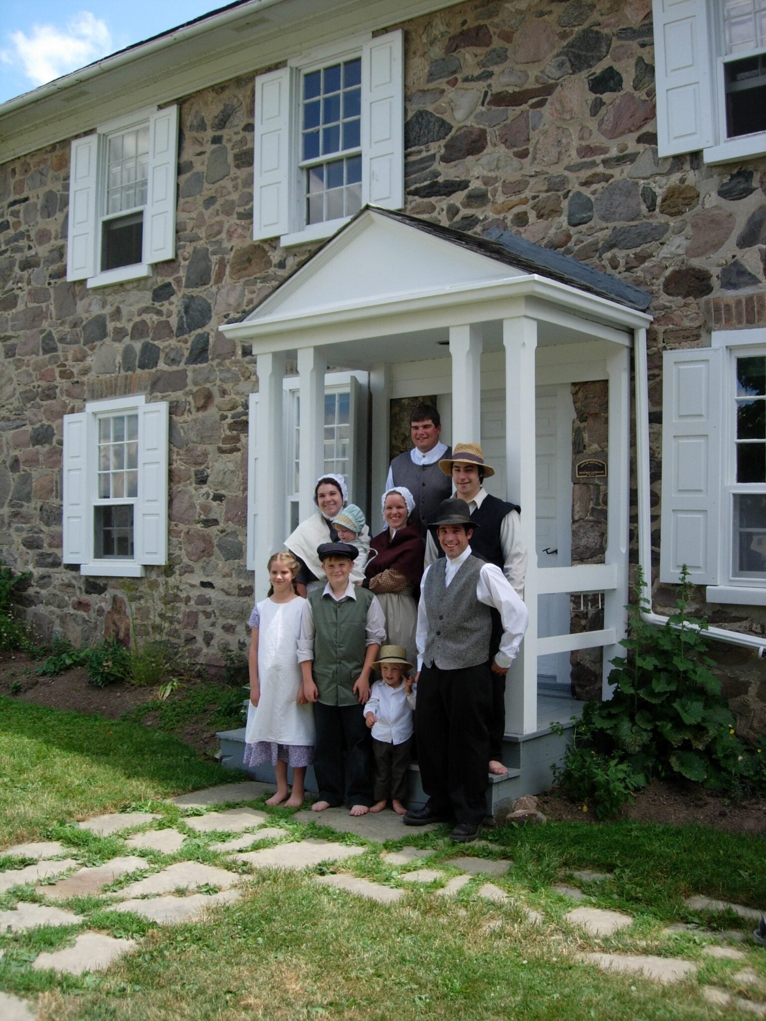A group of actors dressed in historical costumes stand outside brubacher house