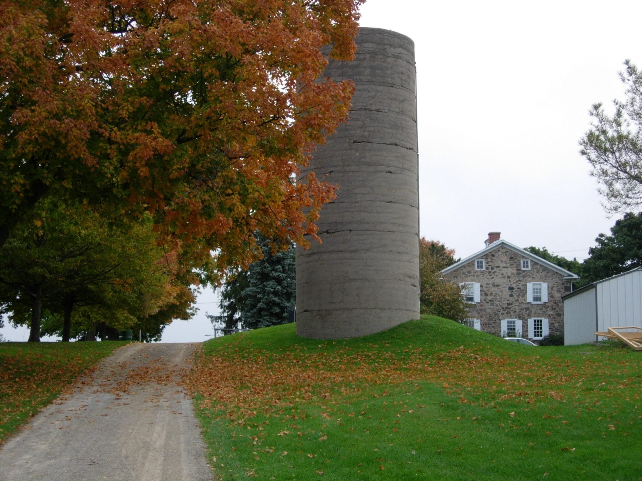 A view of a stone silo, and an tree with orange leaves in fall.